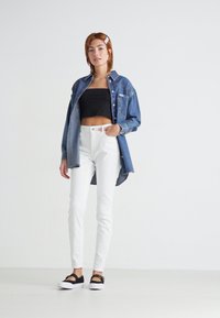 Denim košulja u plavoj boji preko crnog kratkog topa, u kombinaciji s bijelim uskim trapericama i crnim slip-on cipelama s bijelim đonom.