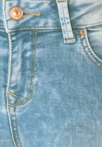 Los pantalones vaqueros de mezclilla azul claro cuentan con un cierre de botón, costuras prominentes y un diseño clásico de cinco bolsillos con un ligero desgastado.