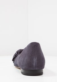 Dark gray suede flat shoe viewed from the back, showing a low black heel and a decorative bow on the side.