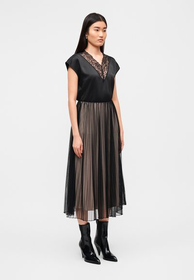 Μαύρο φόρεμα με δαντέλα στο V-λαιμό, κοντά μανίκια και πλισέ διαφανή φούστα. Φορεμένο με γυαλιστερά μαύρα μποτάκια αστραγάλου. Απλός και κομψός σχεδιασμός.