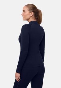 Marineblaues Langarmoberteil aus weichem Stoff, mit hohem Kragen, figurbetontem Schnitt und glatter Textur. Passend mit passenden Hosen kombinierbar.