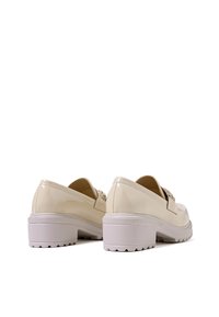 Scarpe in pelle lucida color crema con tacco basso a blocco, punta arrotondata e dettaglio decorativo sul retro. Presentano una suola in gomma bianca texturizzata.