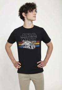 Černé tričko s grafikou Millennium Falcon a textem "STAR WARS 77" v bílé a červené barvě, umístěné na horizontálních barevných pruzích.