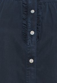 Camicetta blu navy con piastra centrale e quattro bottoni perlacei, dotata di un design arricciato lungo la linea dei bottoni, realizzata in tessuto leggero.