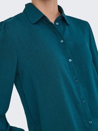 Camicia button-up color verde acqua con colletto, caratterizzata da un tessuto strutturato, pieghe sottili sulle spalle e bottoni azzurri.