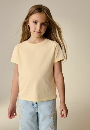 Light yellow cotton t-shirt with short sleeves, paired with light blue denim jeans featuring floral embroidery along the legs.
