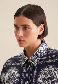 Camicia blu navy con motivo paisley bianco, con colletto strutturato e chiusura a bottoni, realizzata in tessuto liscio.