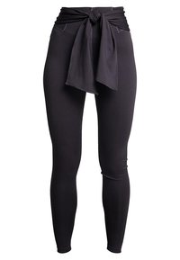 Leggings neri con vita alta, caratterizzati da un accento in tessuto annodato nella parte anteriore e una superficie liscia in tutto il capo.