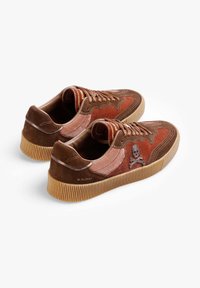 Bruine suède sneakers met oranje accenten, voorzien van een doodskoplogo en een getextureerde rubberen zool. Vetersluiting met contrasterende stikseldetails.
