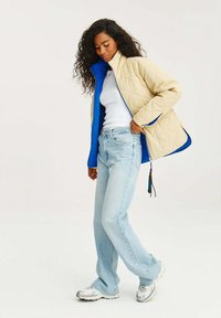 Prošívaná bunda v béžové a modré barvě, s stojáčkovým límcem a zipovým zapínáním. Dvěšena s světle modrými džíny a stříbrnými teniskami.