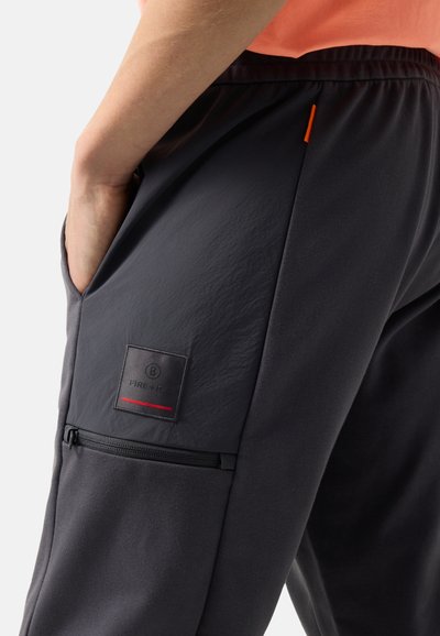 Zbliżenie na osobę noszącą czarne spodnie Fire+Ice, z ręką w bocznej kieszeni i widoczną kieszenią na zamek poniżej.