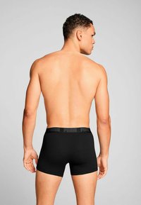 Black boxer shorts made of smooth material with a soft waistband featuring the Puma logo. The garment has a snug fit and minimal design.