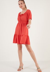 Red puff-sleeve dress with a square neckline, gathered waist, and tiered skirt. Made of textured fabric with a flared hem.