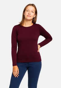 Maglietta bordeaux a maniche lunghe con scollo tondo, design aderente e tessuto morbido, abbinata a jeans blu scuro.