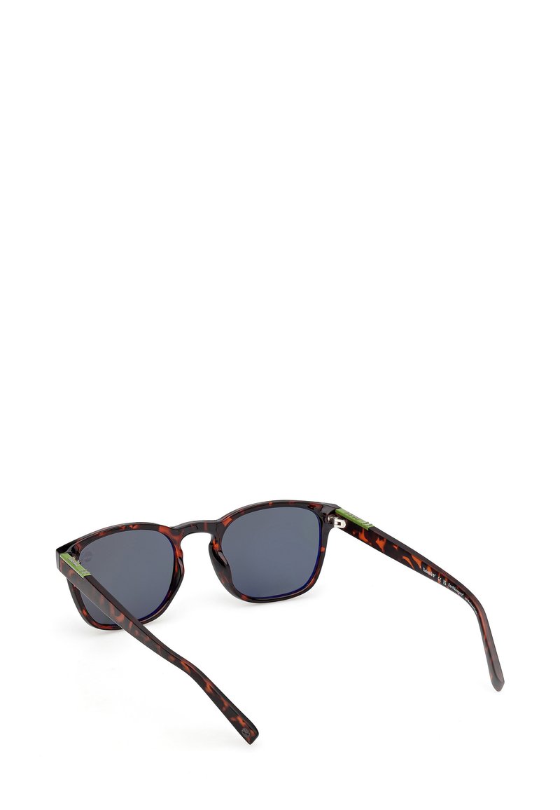 Lunettes de soleil avec une monture en plastique écaille de tortue, verres foncés et accents verts sur les branches. Léger, forme arrondie.