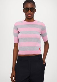Kortermet, cropped genser i rosa og grå striper, laget av mykt strikket materiale. Har en ribbet halslinning og en liten rød etikett på sømmen.