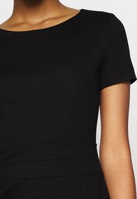 Czarna sukienka z krótkimi rękawami, z okrągłym dekoltem i wyraźnymi szwami. Tkanina ma gładką fakturę i dopasowany krój.