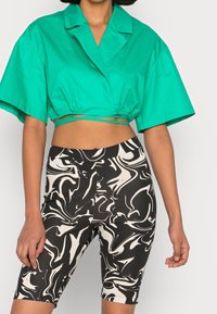 Chemisier bleu sarcelle court avec col et liens latéraux, associé à un short de cyclisme noir et blanc à imprimé marbré, en tissu extensible.