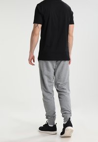 Svart kortärmad t-shirt i kombination med ljusgrå träningsbyxor, som har en avslappnad passform och elastiska ärmslut. Svarta sportskor fulländar outfiten.