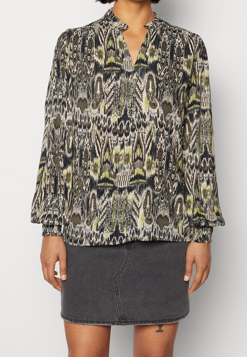 Blouse à manches longues avec motif abstrait noir, blanc et vert, associée à une jupe en denim gris foncé, portée par une personne des épaules jusqu'au milieu des cuisses.