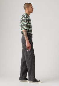 Camiseta a rayas en verde, negro y blanco, combinada con pantalones cargo en carbón. Presenta un corte holgado, bolsillos frontales y zapatillas negras.
