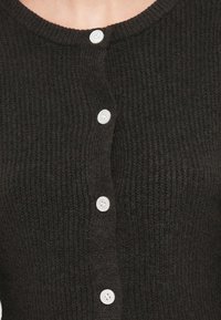 Σκούρο πλεκτό πουλόβερ με στρογγυλή λαιμόκοψη, υφή υφάσματος και πέντε λευκά κουμπιά στο μπροστινό μέρος.