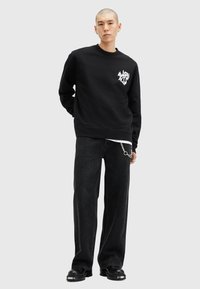 Sort sweatshirt med rund hals og hvid grafik på brystet, parret med løstsiddende sorte jeans og kraftige sorte støvler.