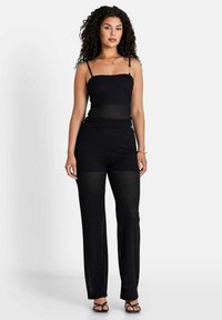 Zwart twee-delig outfit met een mouwloze, aansluitende top met dunne banden en wijdvallende broeken, beide gemaakt van een getextureerde, open gebreide stof.