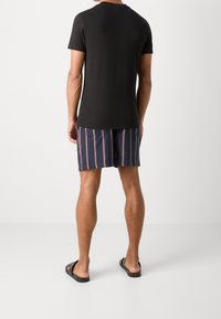 Svart bomullströja med korta ärmar, matchad med marinblå shorts med vertikala ränder i röd och vit. Bärs med svarta flip-flop-sandaler.