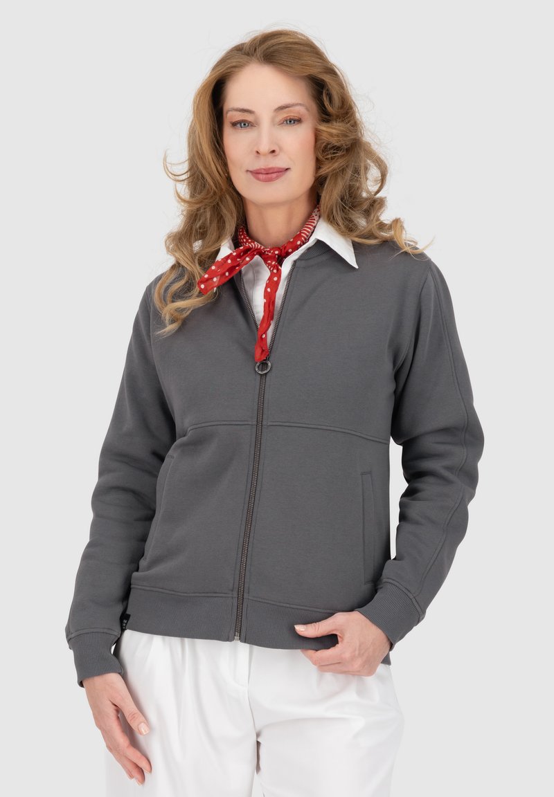 Felpa grigia con zip realizzata in pile, caratterizzata da polsini e orlo a coste, con un design di cucitura sottile. Indossata sopra una camicia bianca con colletto.