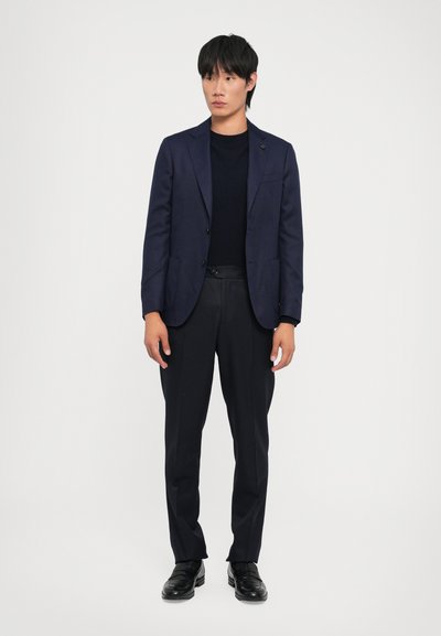 Navy blazer over a black crewneck sweater, paired with black trousers and loafers. Smooth fabric, tailored fit, and minimal detailing.