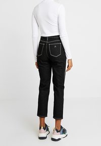 Svarta högmidjade jeans med rak benklippning, med bakfickor i brunt stygn och bärs med mångfärgade sneakers.