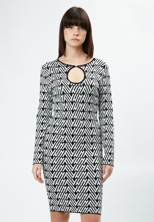 Vestido de punto en blanco y negro con un patrón geométrico, mangas largas y un detalle de escote con abertura. Silueta ajustada.