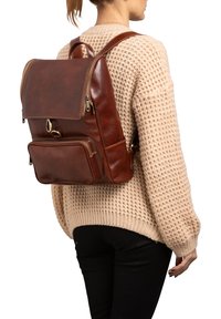 Zaino in pelle marrone con un design strutturato, dotato di una tasca frontale con zip, spallacci regolabili e dettagli in hardware color oro.