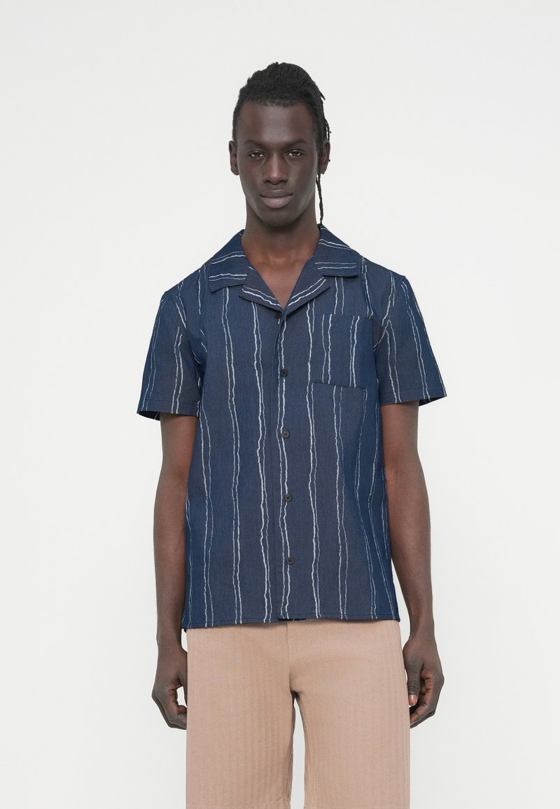 Πουκάμισο με κοντά μανίκια σε ύφασμα ναυτικού μπλε με άσπρες κάθετες ρίγες, με γιακά και τσέπη στο στήθος, κλασικό κουμπωτό εμπρός.