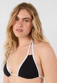 Top de bikini en forma de triángulo negro con tirantes blancos, con un borde volado en la parte inferior. La tela parece suave y cuenta con lazos ajustables.