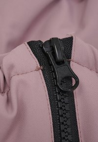 Rosa Stoff mit einer strukturierten Oberfläche, ausgestattet mit einem schwarzen Reißverschluss mit einem glatten Ziehgriff und kontrastierendem schwarzen Nähten entlang der Kante.