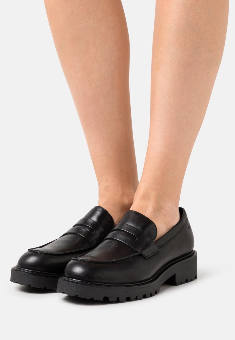 Mocassins en cuir noir à finition lisse, avec un détail double boucle, une semelle épaisse en caoutchouc et un design à bout arrondi.