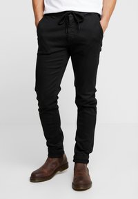 Zwarte casual broek met een trekkoord in de taille, slim fit en zijzakken, gecombineerd met bruine enkellaarzen. Glad textuur, geen zichtbare patronen.