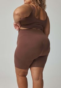 Brązowy, jednolity sportowy biustonosz i szorty z wysokim stanem, wykonane z gładkiego, elastycznego materiału. Charakteryzują się dopasowanym krojem i szortami sięgającymi kostek.