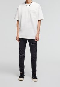 Camiseta blanca de gran tamaño con un bolsillo en el pecho, combinada con jeans negros desgastados que tienen desgastes, y zapatillas altas negras con una suela blanca.