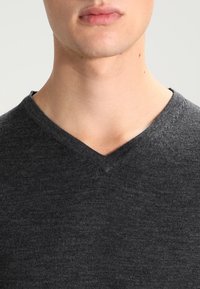 Sweter w kolorze antracytowym z dekoltem w serek, wykonany z miękkiej tkaniny, z prostym, teksturowanym wzorem, bezszwowym kołnierzem i bez widocznych logo.