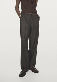 Brown tailored trousers with a high waist, wide legs, and pleats. Made from a textured fabric, paired with dark brown moccasin-style shoes.