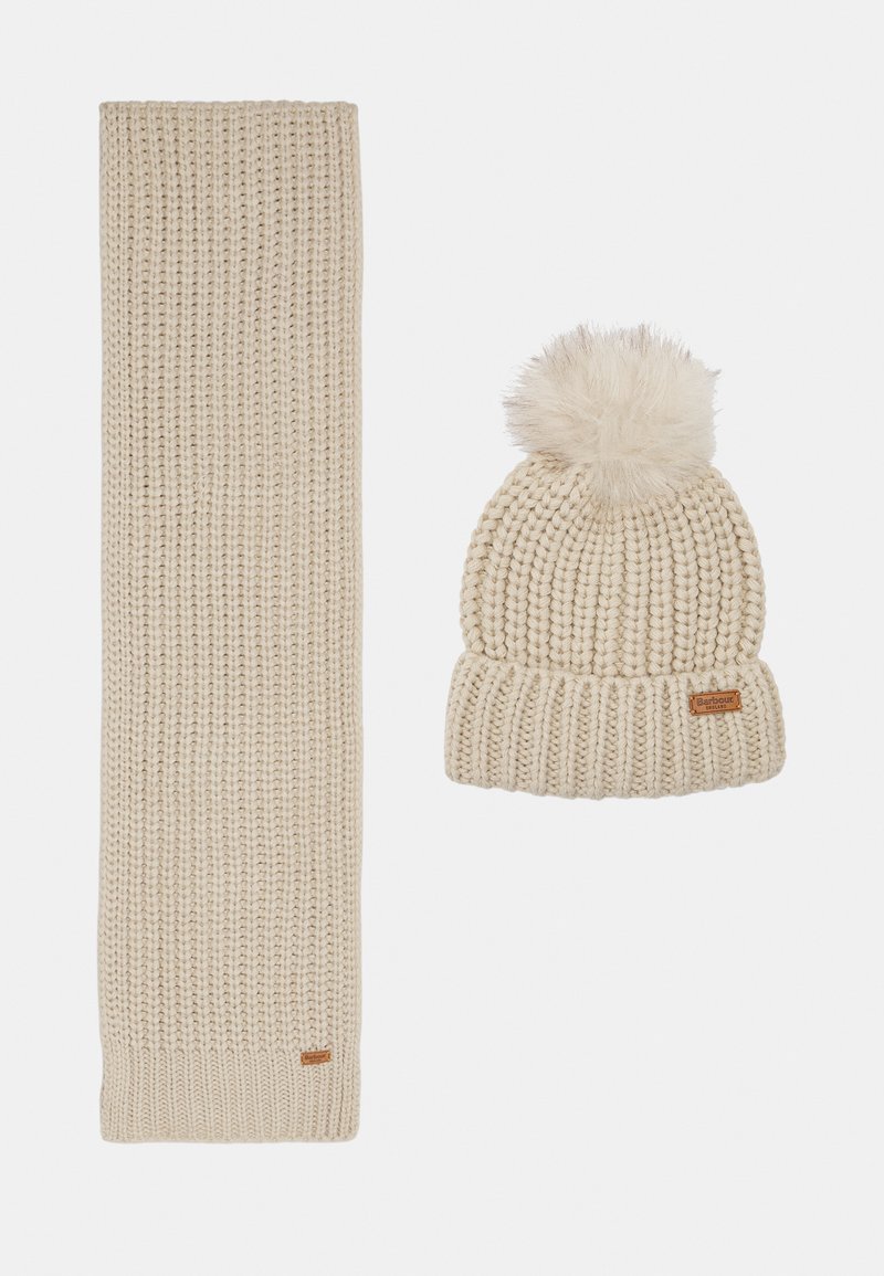Beige gebreide sjaal en muts set. De muts heeft een fluffy pompon en een ribbelontwerp. Beide items zijn voorzien van een leren label.