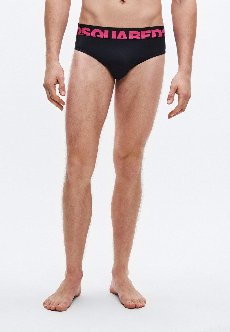 Mustad ujumispüksid laia fuksia värviga vöökohaga, millel on logo "DSQUARED2." Materjal tundub sile, lõige on tihe.