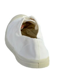 Zapatilla de lona blanca con puntera redondeada, suela de goma y costuras mínimas. La parte superior abierta revela el forro interior y los detalles del cordón.