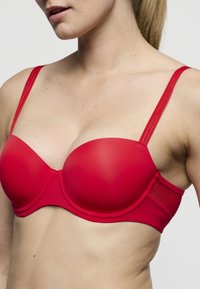 Rode gewatteerde beha met gladde stof, dunne verstelbare bandjes en een afgeronde cupvorm. Heeft een naadloos ontwerp met een effen kleurafwerking.