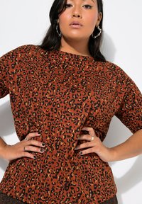 Top corto marrón de manga corta con un patrón de estampado de leopardo en negro y dorado. Material de algodón con un ajuste relajado y cuello redondo.