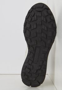 Suela de zapato de goma negra con patrones de dibujo profundos, bordes curvados y un logo en relieve. Superficie texturizada para mejorar el agarre y la tracción.