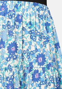 Jupe fleurie avec taille froncée, arborant un motif floral bleu et violet sur un fond clair, fabriquée à partir d'un tissu doux.